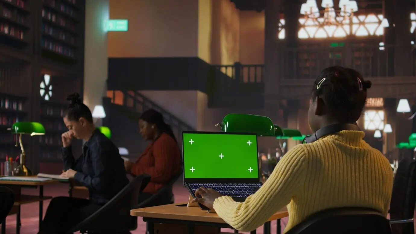 Ein Schulkind im Vor-Teenageralter arbeitet in der Bibliothek mit einem Greenscreen an einer Schulaufgabe.